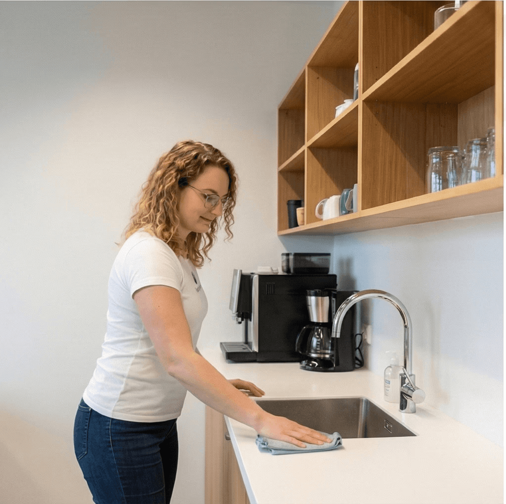 Starfsmaður að þrífa vask og borðplötu í kaffistofu fyrirtækis