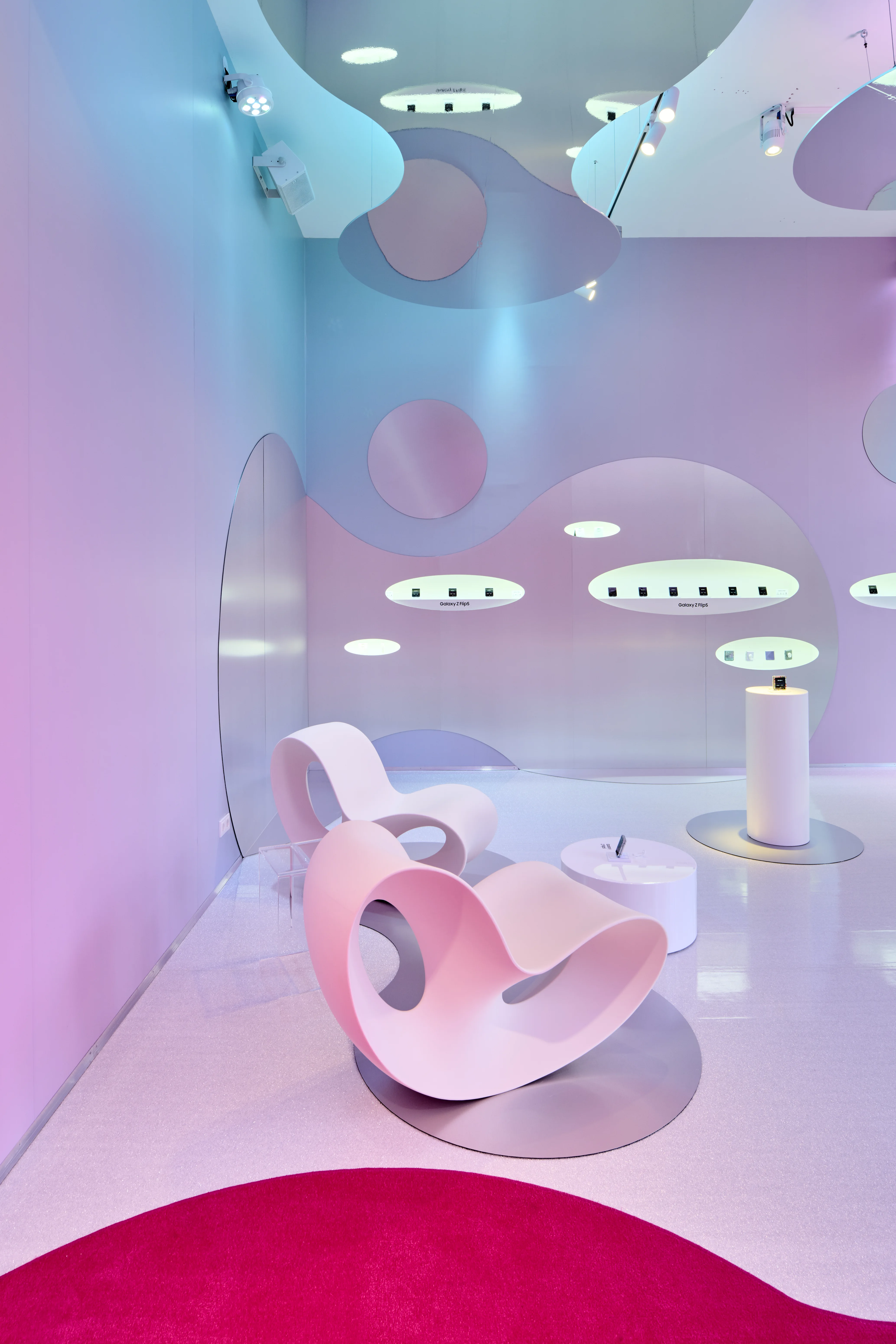 Pastel gradient room with sculptural rocking chairs and oval wall niches holding Galaxy Z Flip phones at the Samsung pop-up.