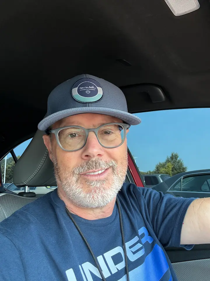 Stuart smiling in car with blue T-shirt and baseball cap.