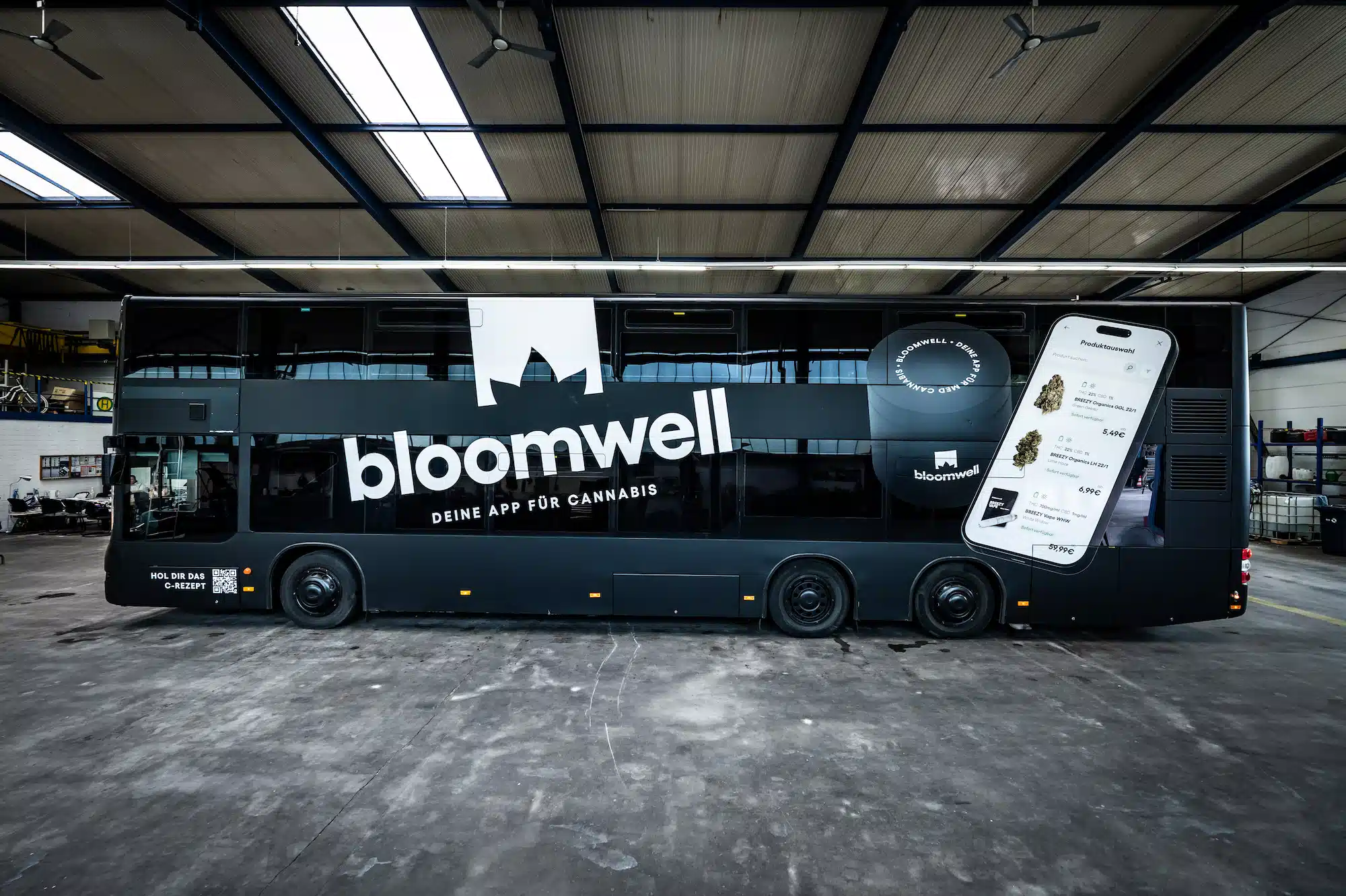 Bloomwell Cannabis App – black double-decker bus with side branding and app visual in a warehouse