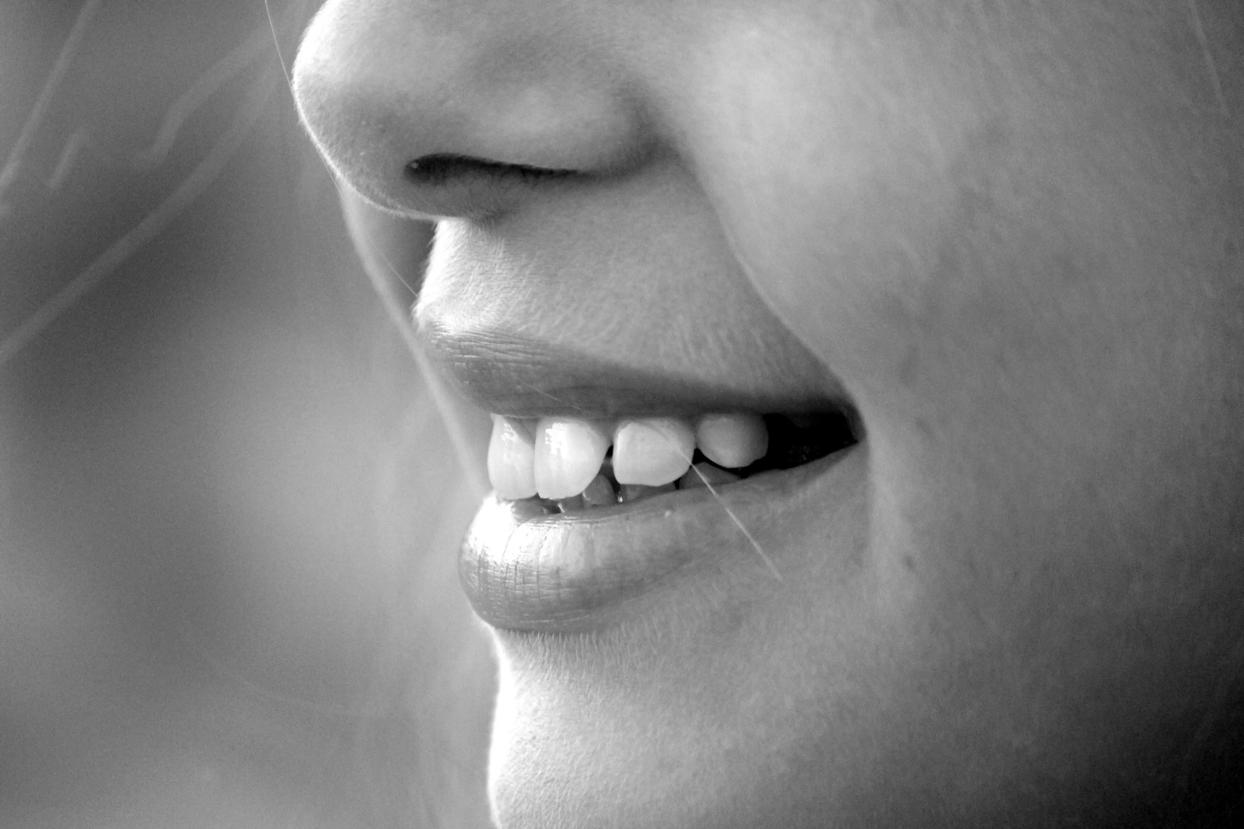 Close-up of a smiling person's mouth, highlighting white teeth and a joyful expression in black and white.