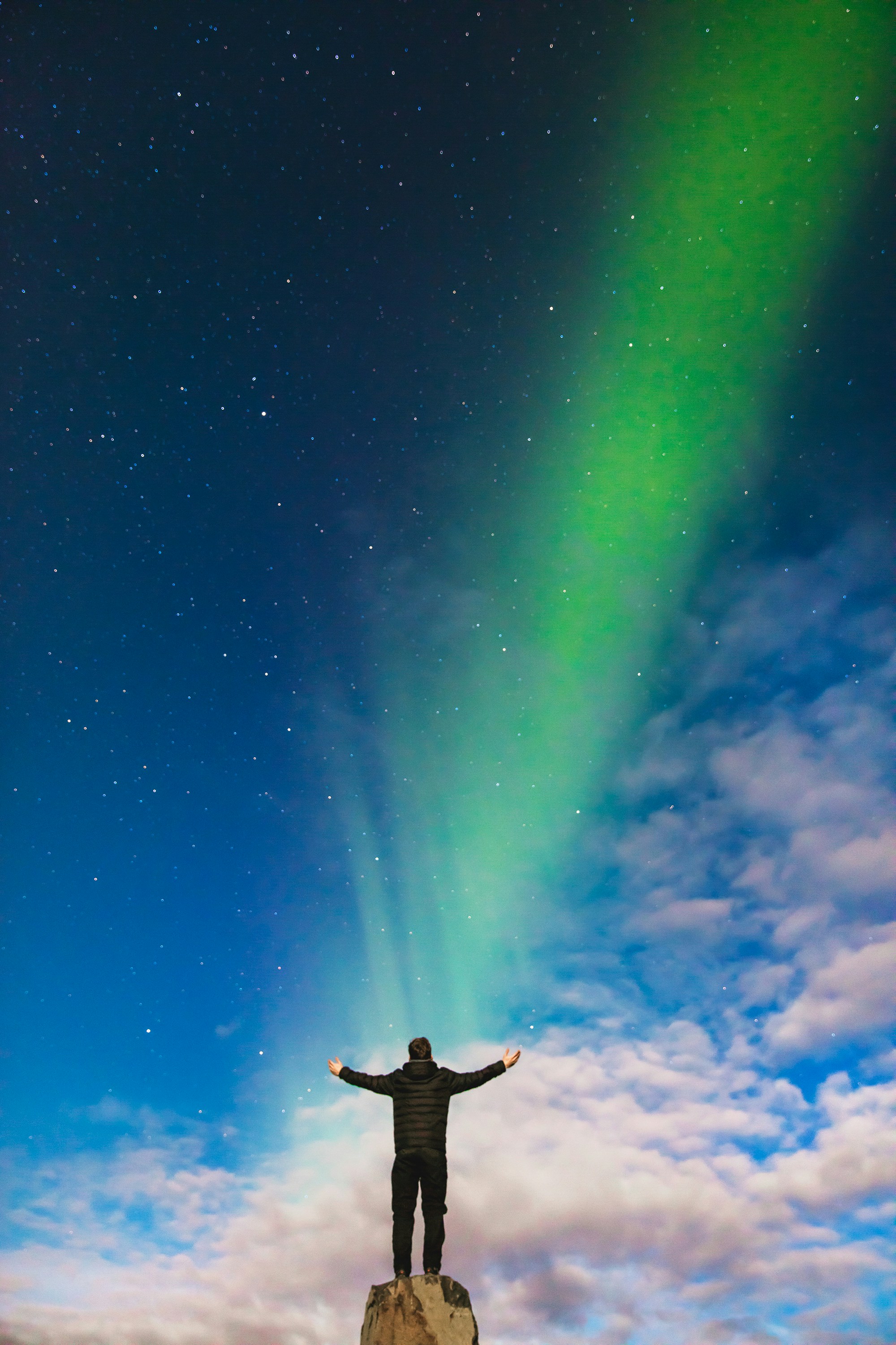 Person standing on a rock with arms outstretched, facing a vibrant sky illuminated by green aurora lights, symbolizing the power of purposeful writing to create impactful and results-driven content.