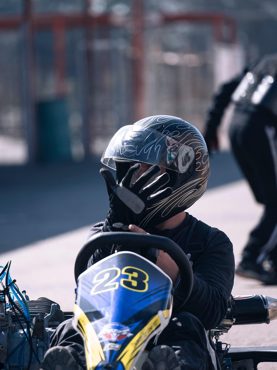 A young person with curly hair smiles at the camera while sitting in front of a laptop against a dark background.