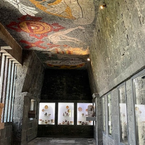 Silid na bato na may mga display case ng palayok, kisame na mosaic na may mga hugis na geometric, at dim na ilaw.