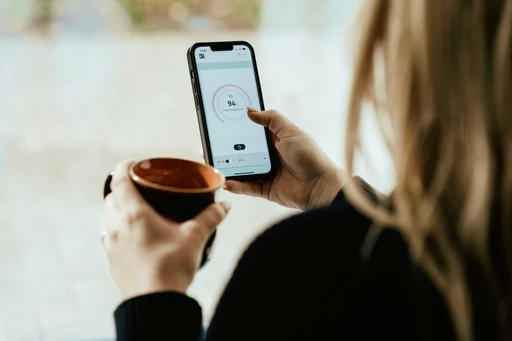 Eine Person, die eine Tasse Kaffee hält und am Handy scrollt.