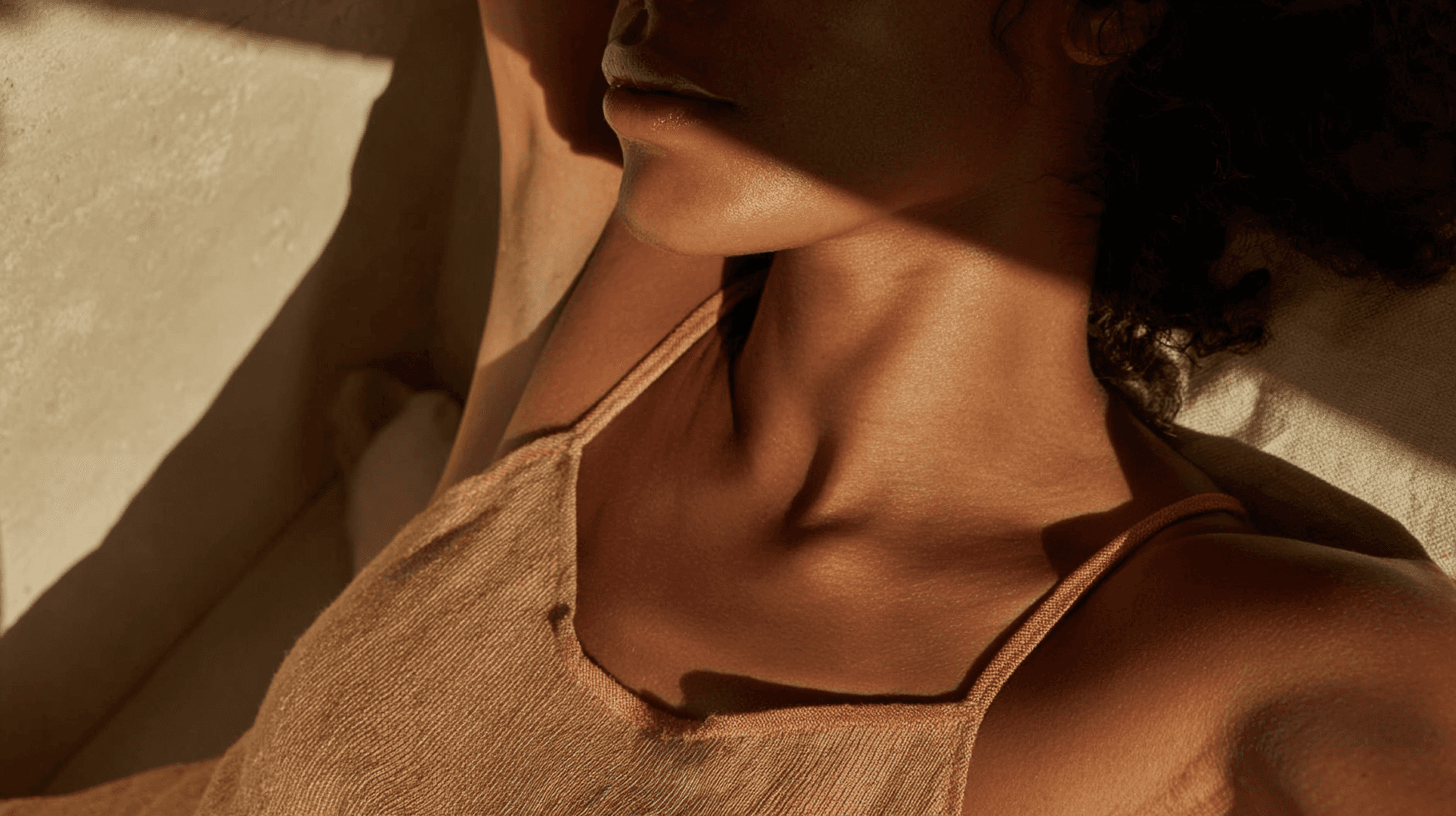 Close-up of a person’s neck and jawline in warm natural light, with soft shadows emphasizing skin texture and contours.