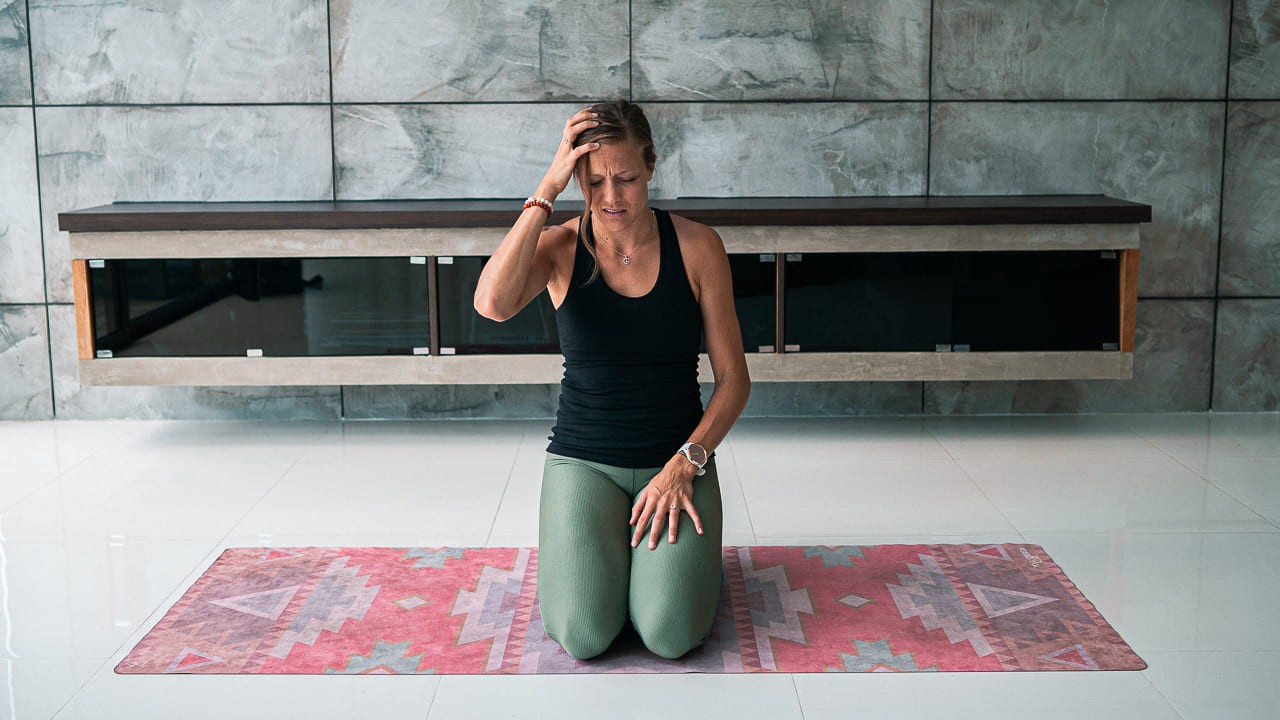 Bre holding her head looking stressed on the yoga mat, ready to practice and find stillness.