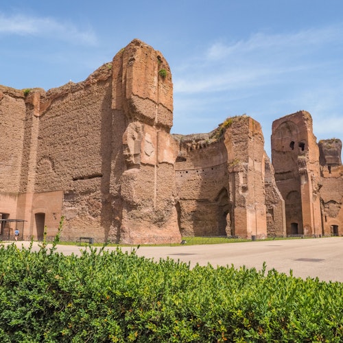 在晴朗的蓝天下，古老的砖瓦遗址有巨大的拱门和墙壁遗迹，周围环绕着绿植。