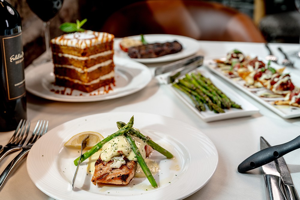 Fish with asparagus, a layered cake and side dishes on a white tablecloth at Eddie Merlot's