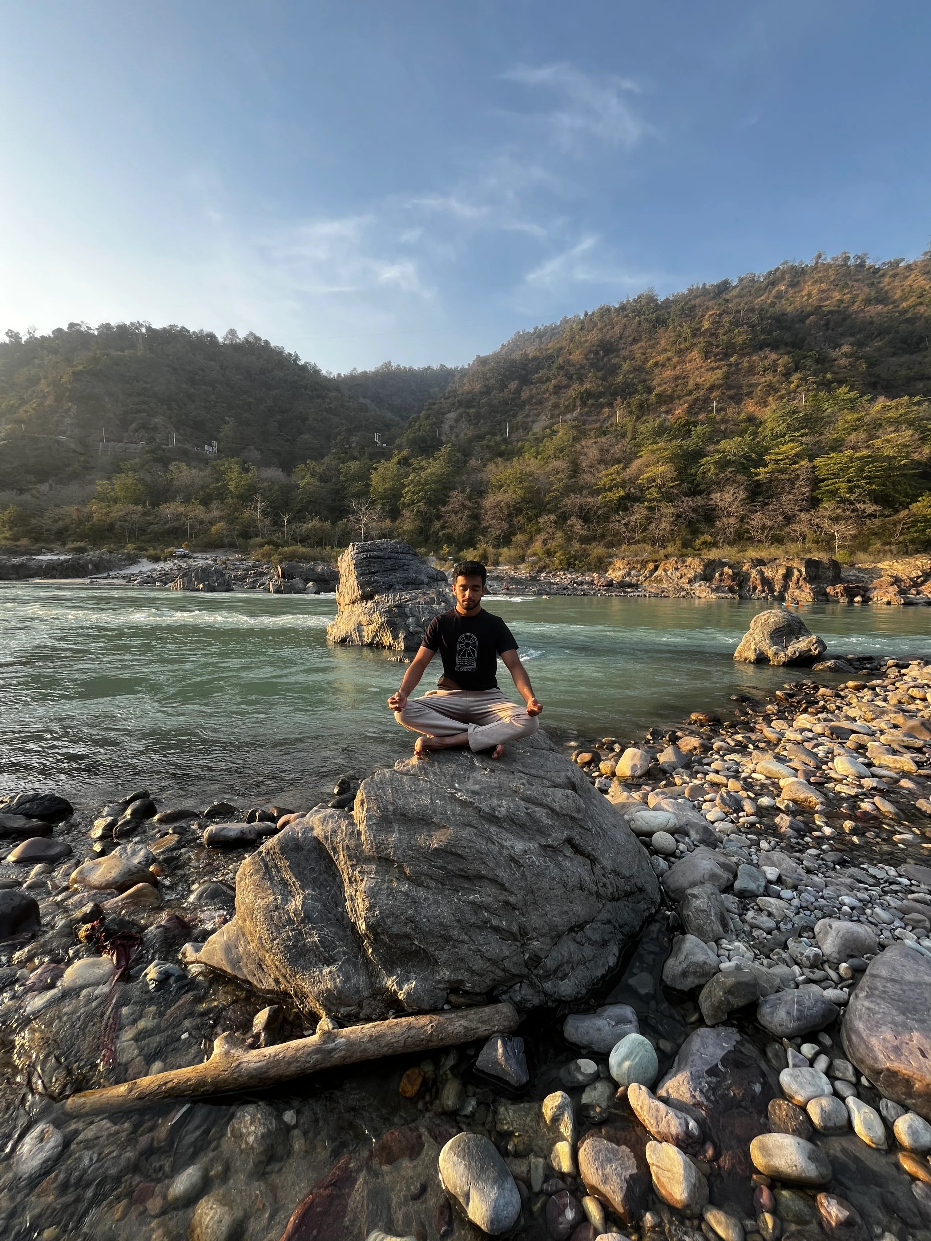 A smiling man with curly hair and glasses stands in a warmly lit room filled with decor and plants.
