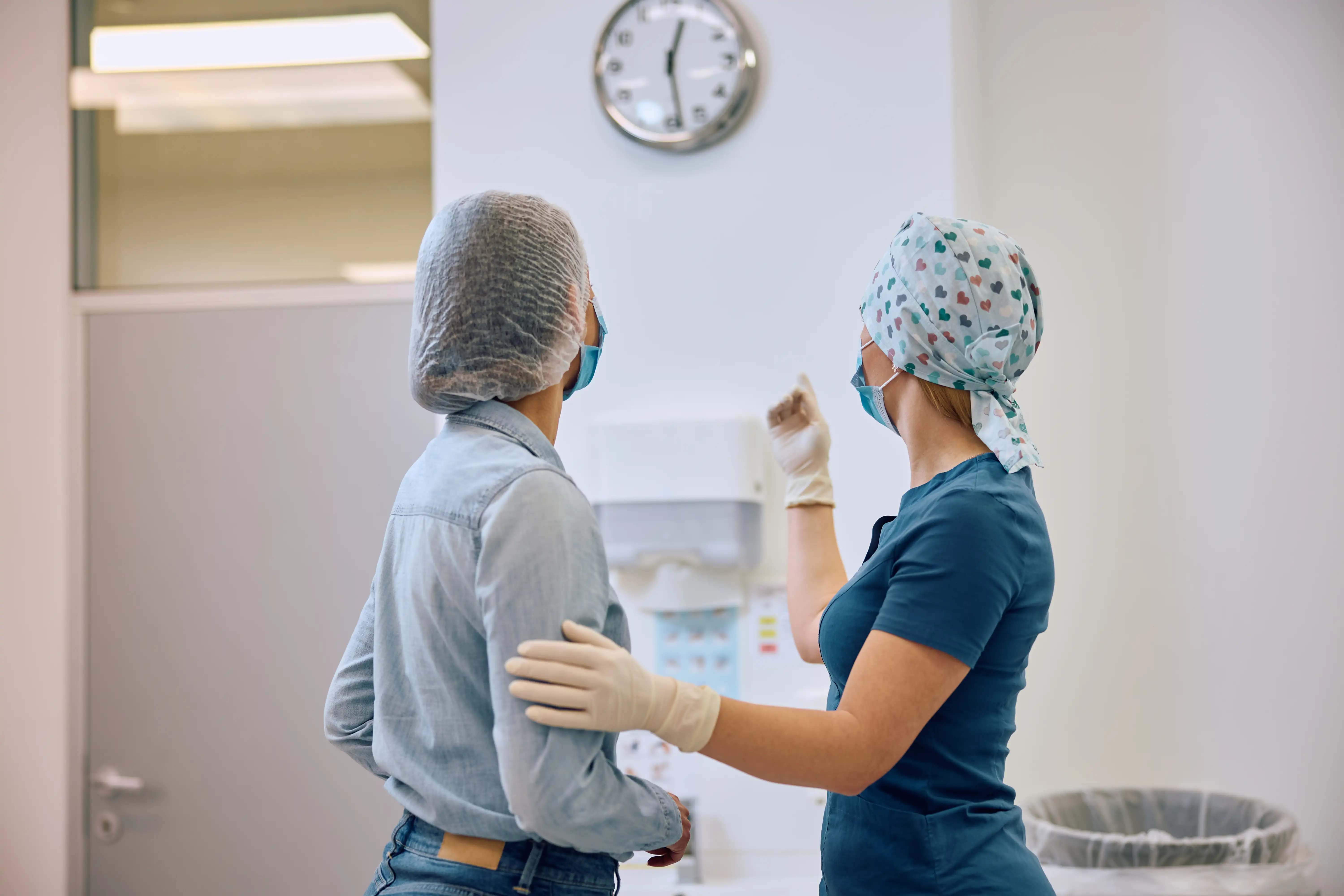 Nurse providing patient care under a wall clock, illustrating unpaid off-the-clock work and missed break violations in California health care facilities