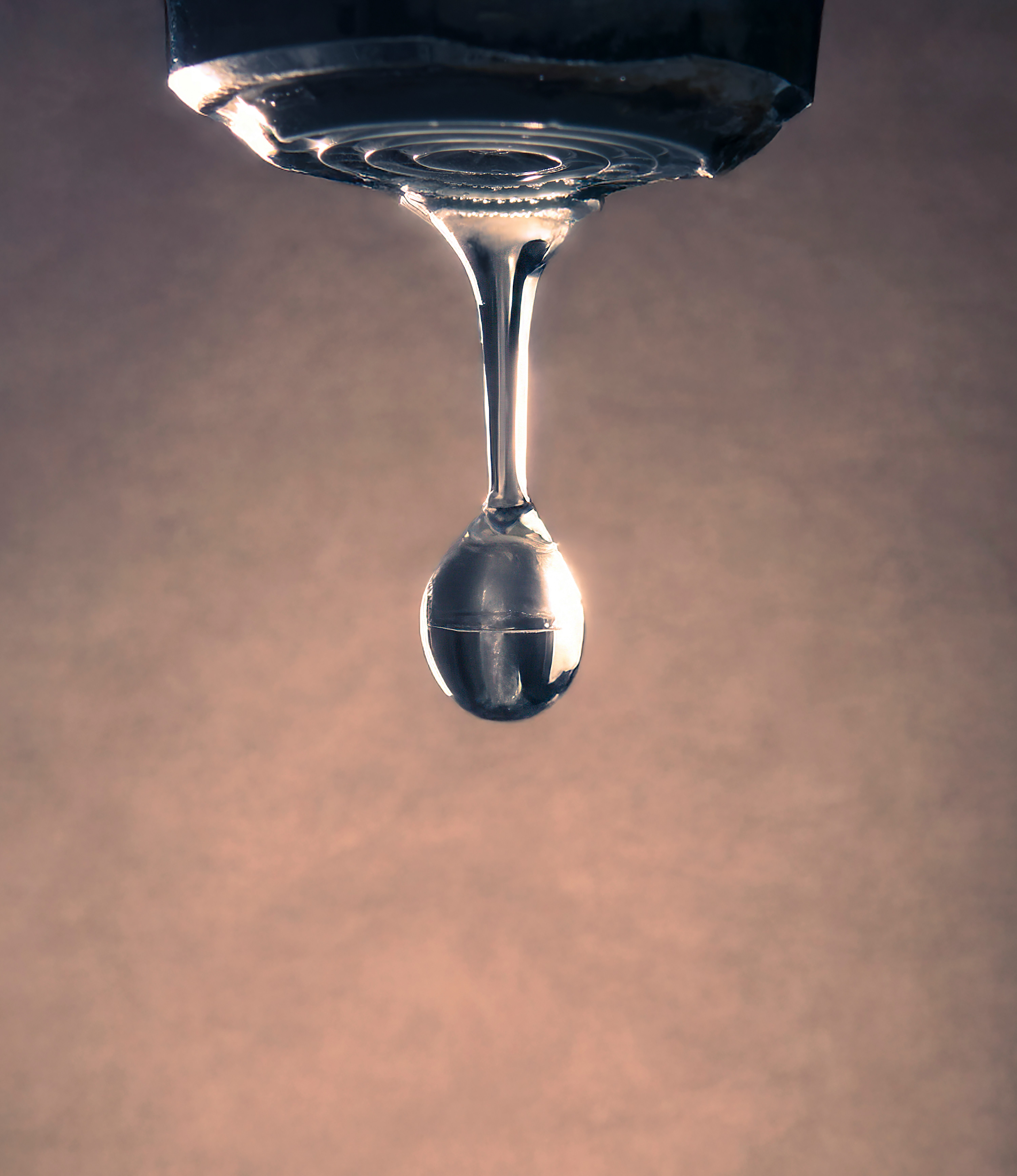 A water drop forms from a faucet.