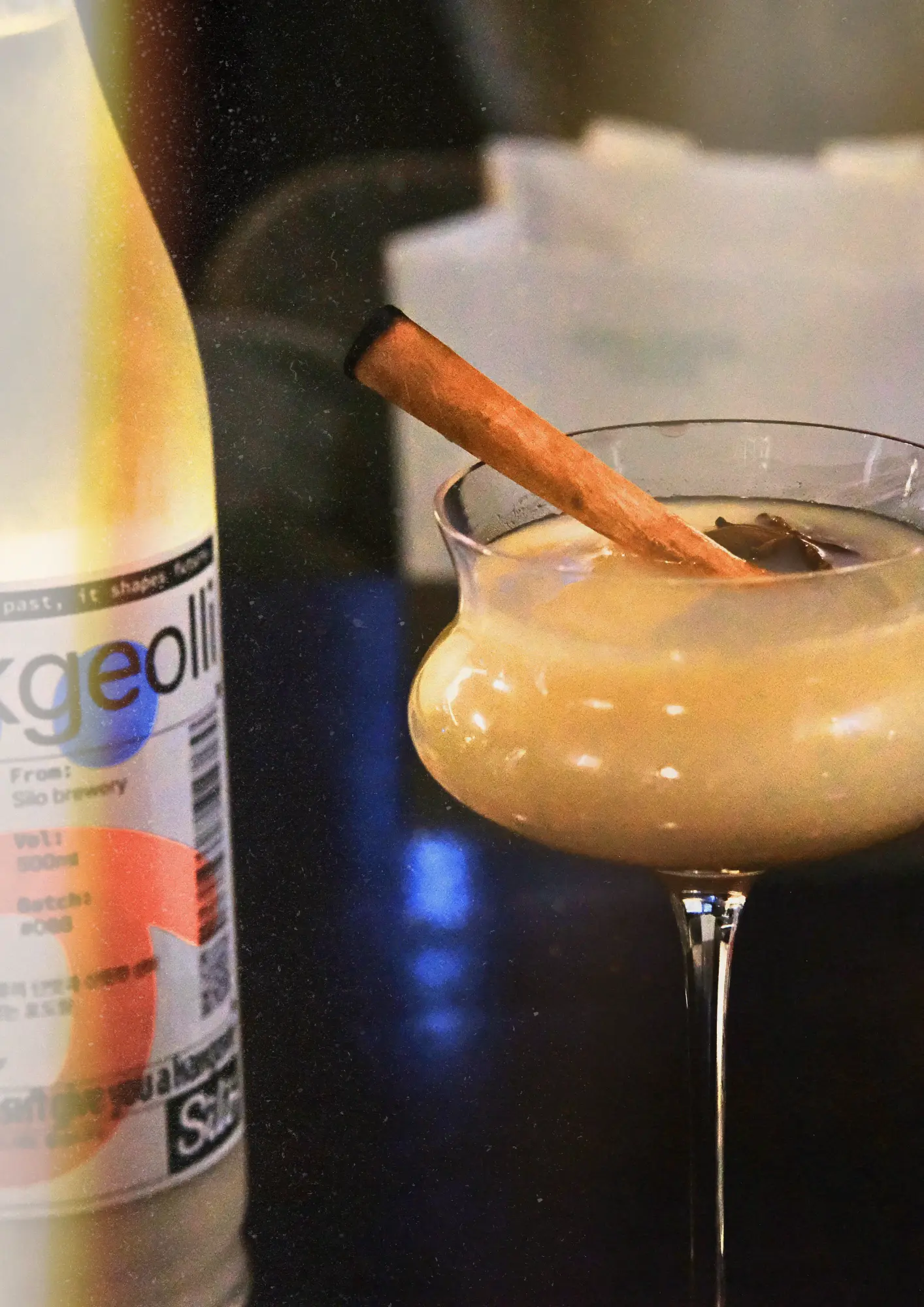Koktajl na bazie makgeolli w eleganckim kieliszku na nóżce, udekorowany cynamonem i gwiazdką anyżu. Po lewej stronie stoi butelka makgeolli z browaru Silo Brewery.