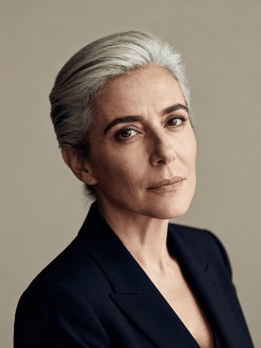 Studio portrait of a woman with short gray hair wearing a dark blazer, facing the camera against a neutral background.