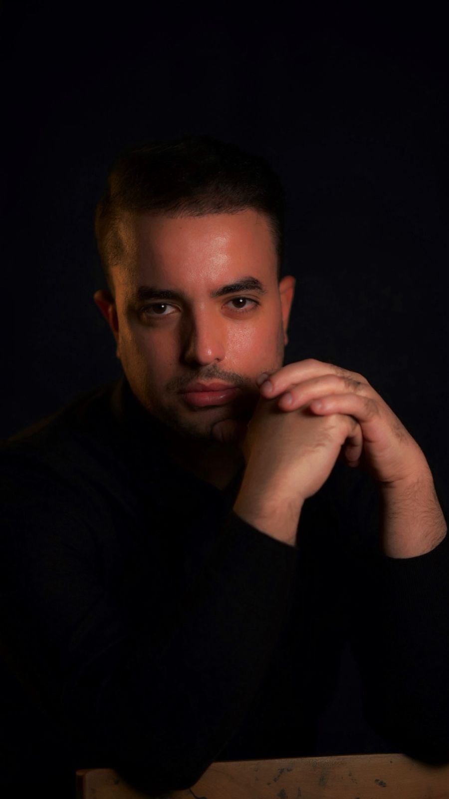 a man wearing a black top with a black background with his hands visible on screen