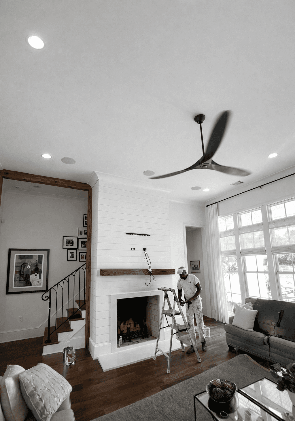 A modern, luxury beachfront villa with large glass windows and balconies overlooks a rocky shoreline, surrounded by palm trees at sunset.