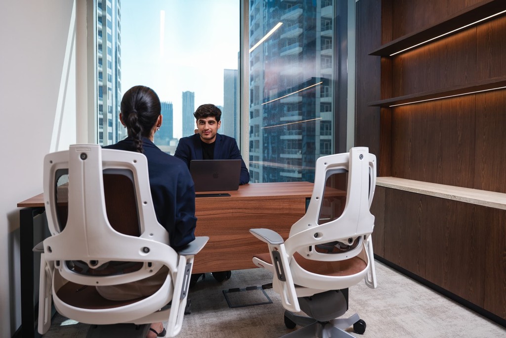 High-capacity shared work zone in serviced office spaces in Dubai with modular desks, built-in pantry, and overhead lighting.