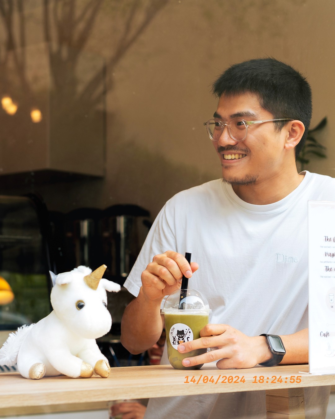 Client souriant tenant un bubble tea matcha chez GUTEA Paris, à côté d'une peluche licorne.