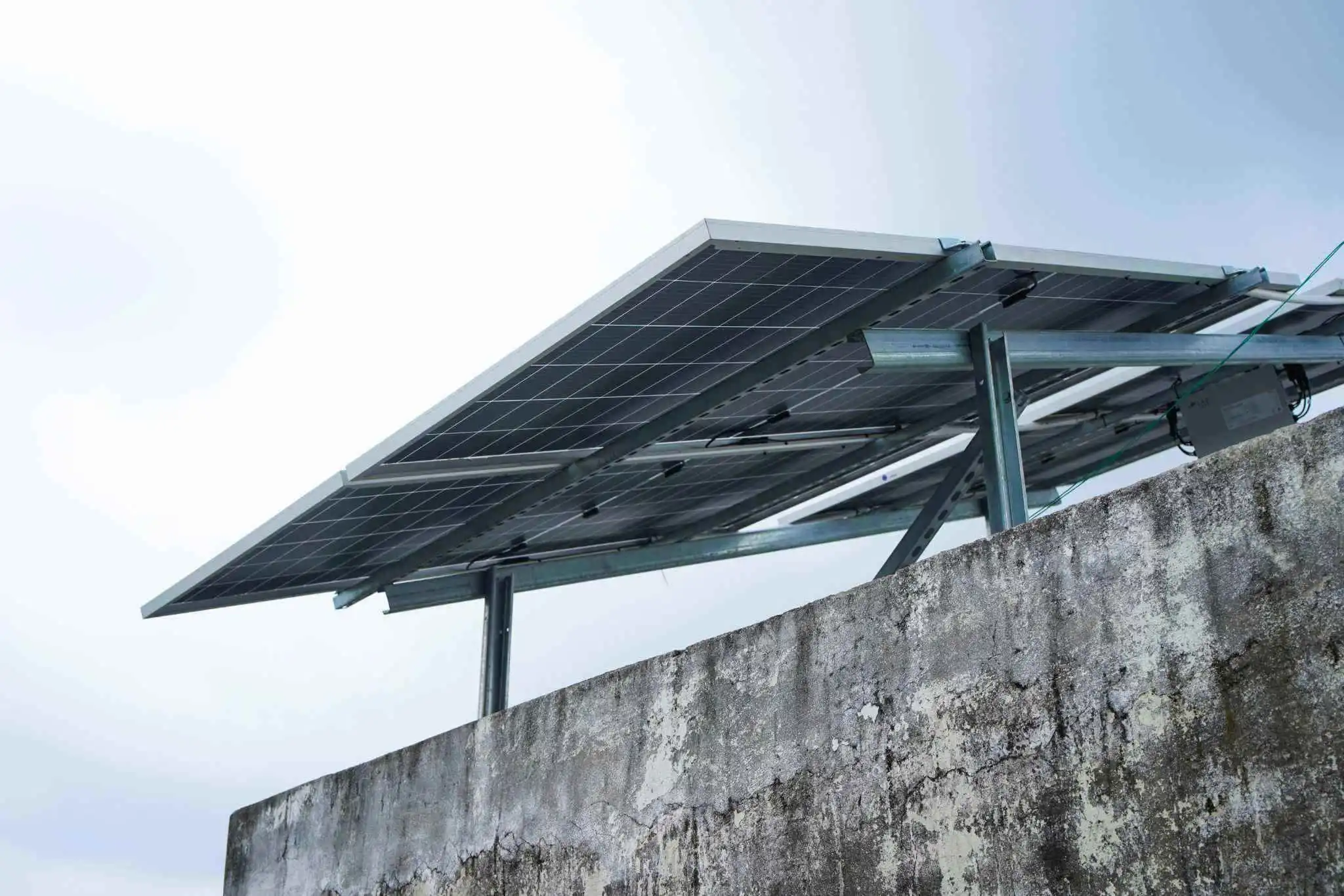 Solar panels on a concrete wall under a pale sky.