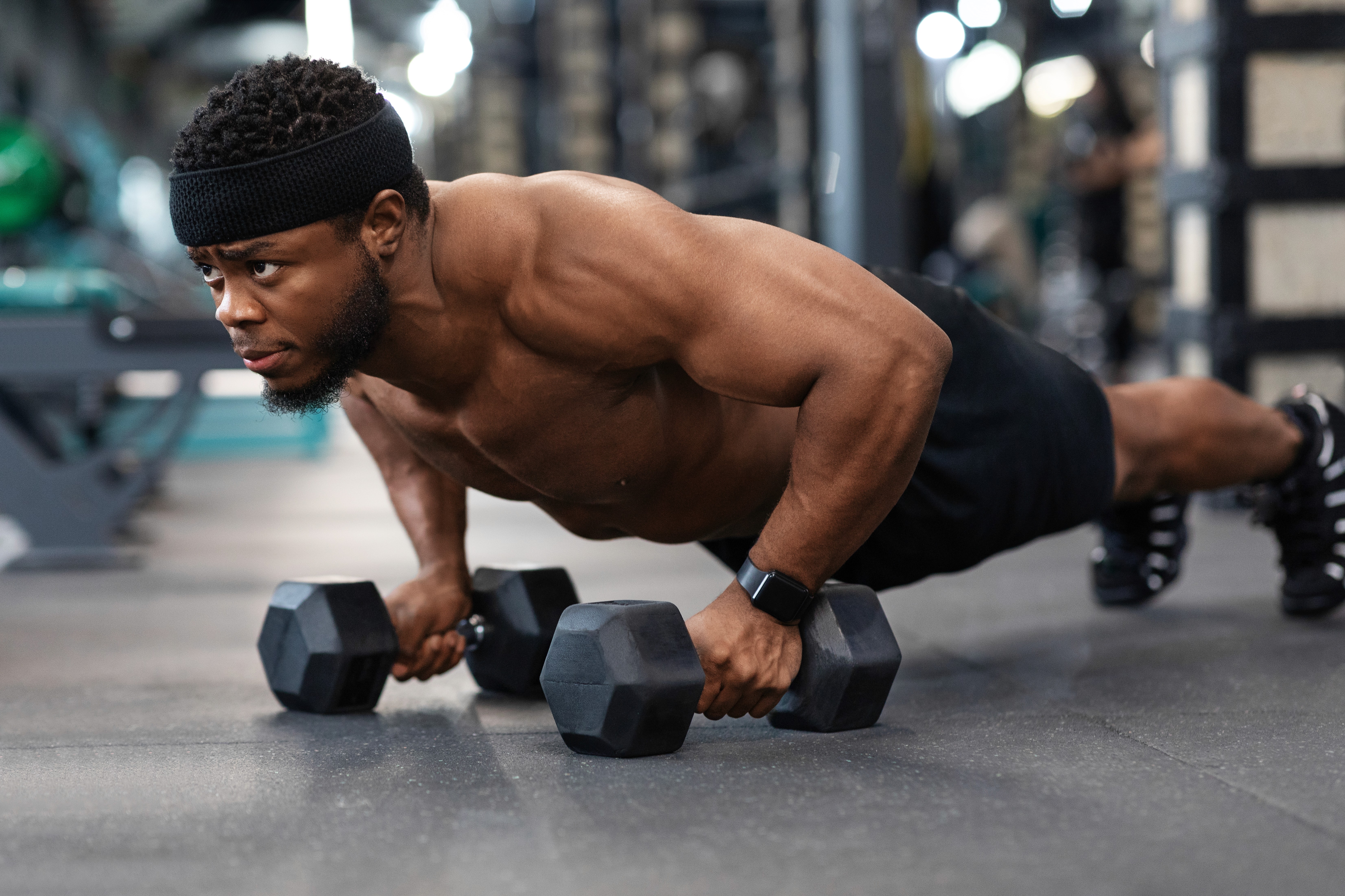 Determined sweaty woman performing push-ups with dumbbells in intense gym workout.