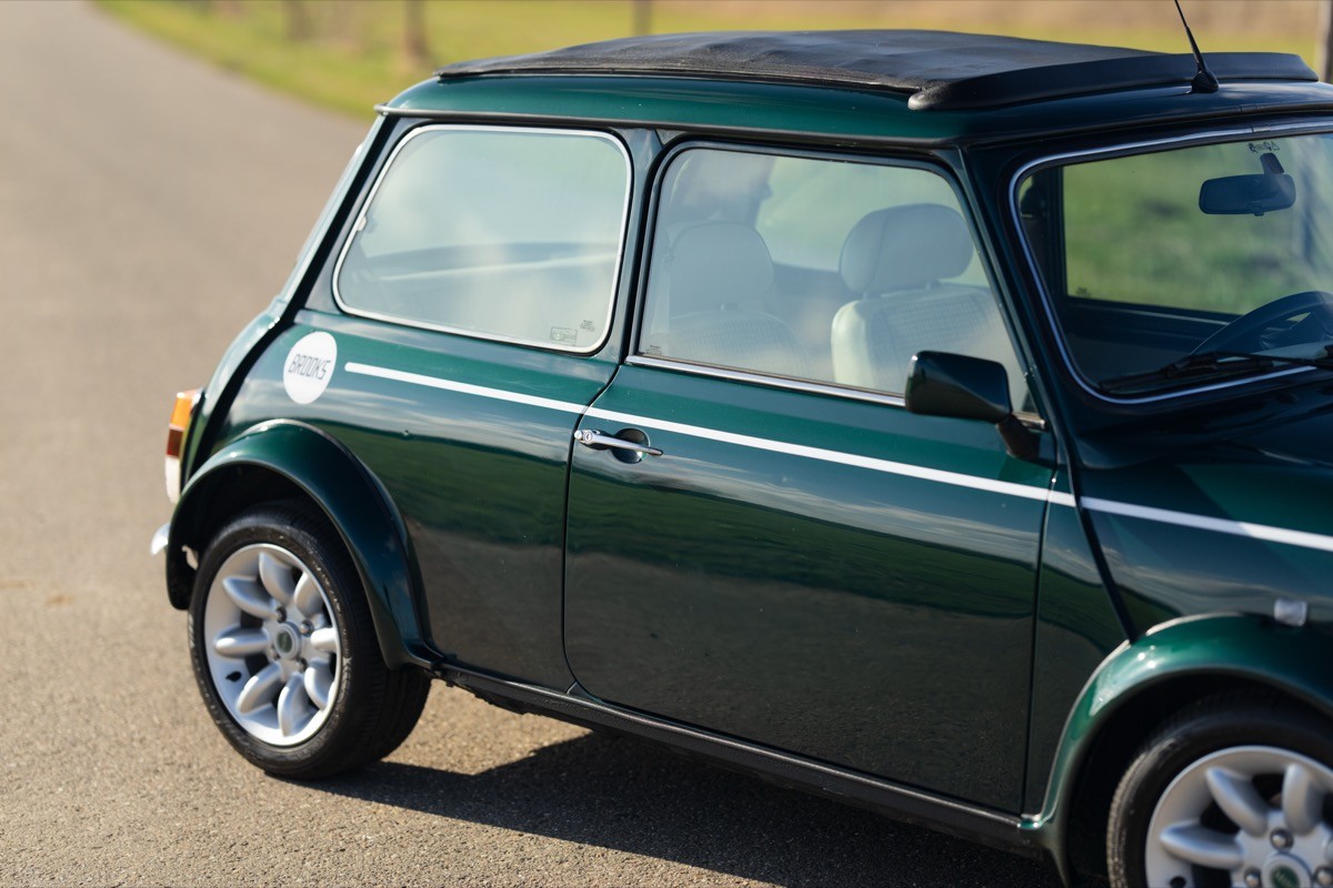 A green classic car parked on a country road, showcasing its stylish curves and shiny wheels.