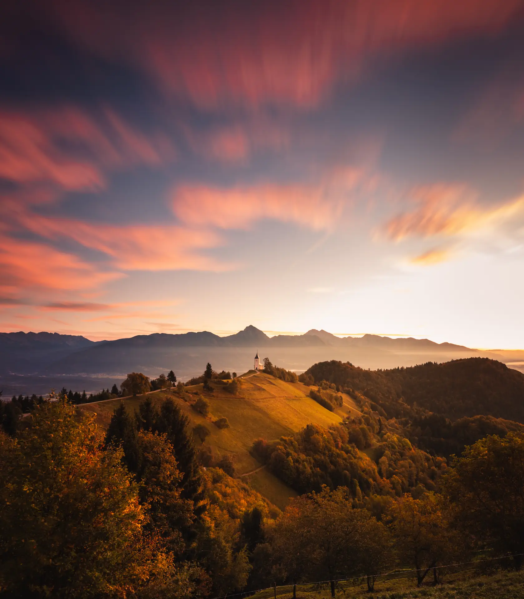 A stunning sunset over rolling hills at Jamnik, Slovenia, with vibrant clouds and warm light illuminating the landscape.