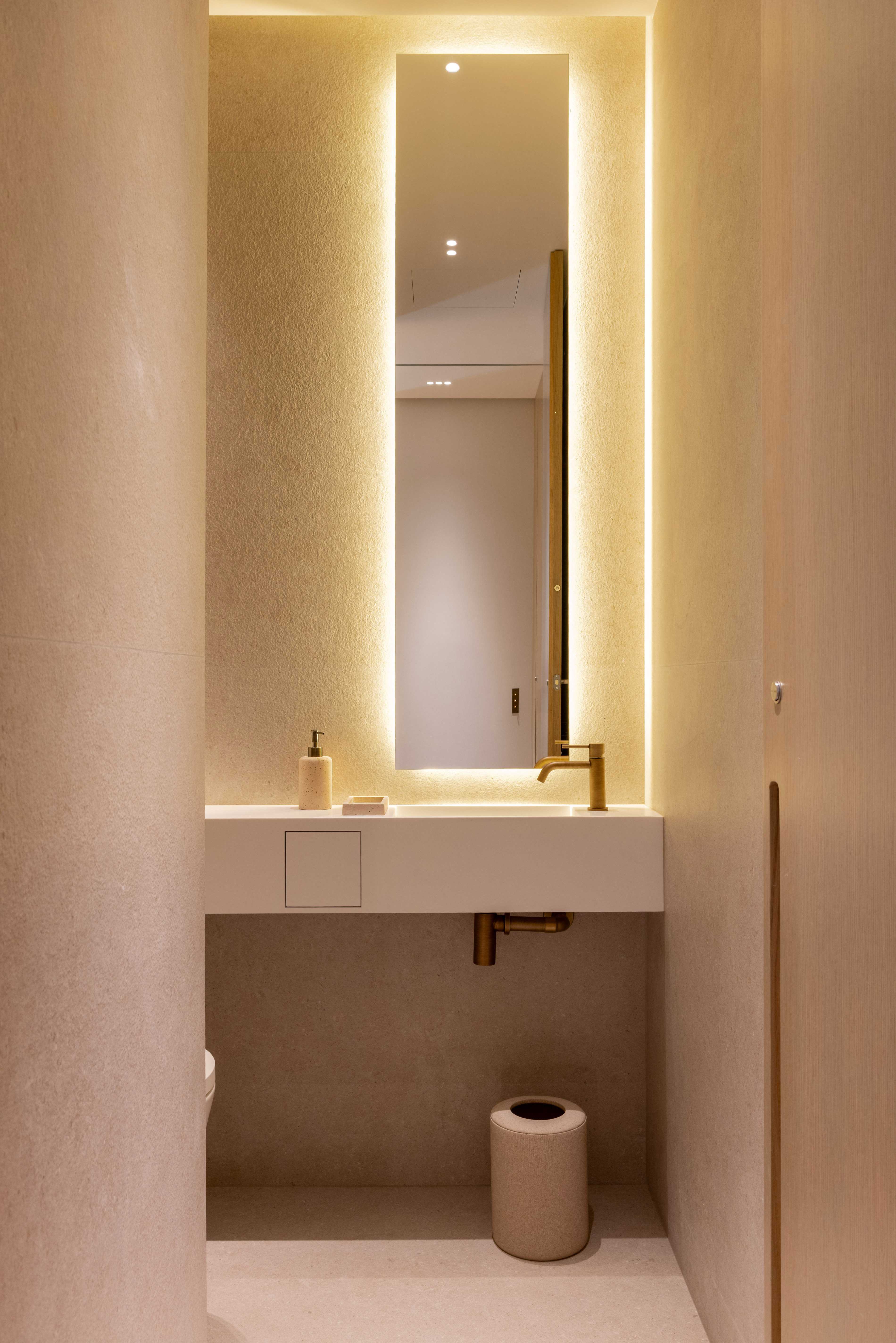 Toilettes invites avec vasque murale, miroir retroeclaire, robinetterie doree et tons rose poudre