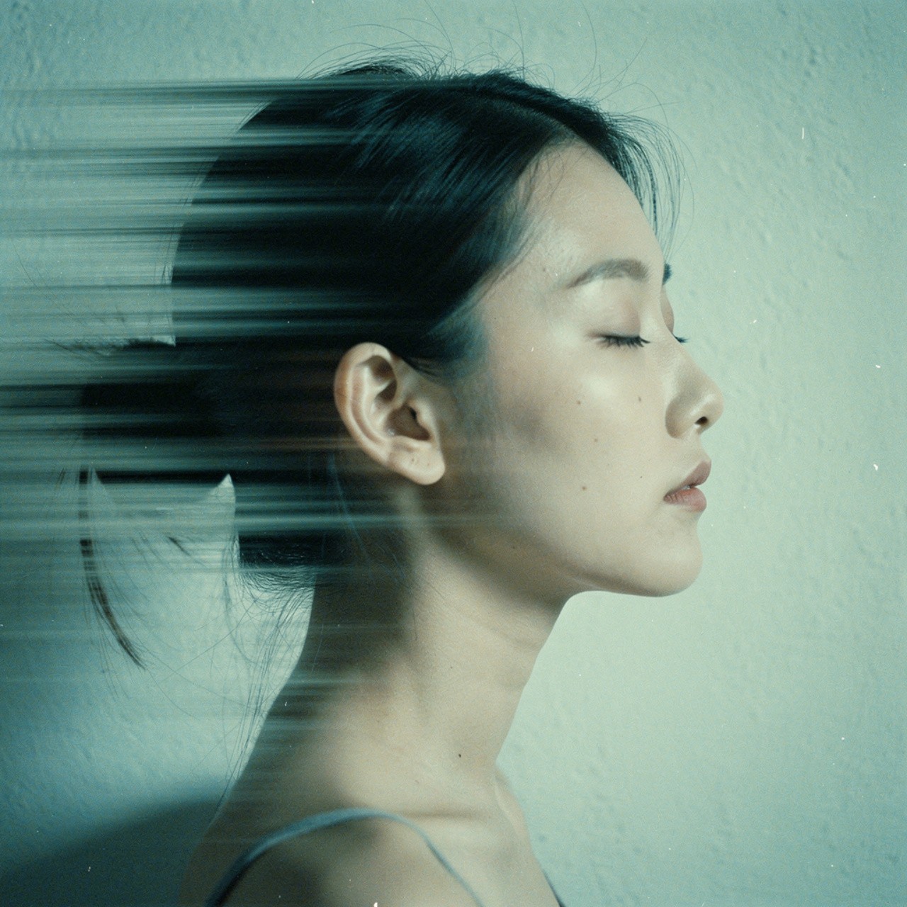 Side profile of a woman with closed eyes, hair blurred by movement, against a muted background. The image conveys a sense of calm and introspection.