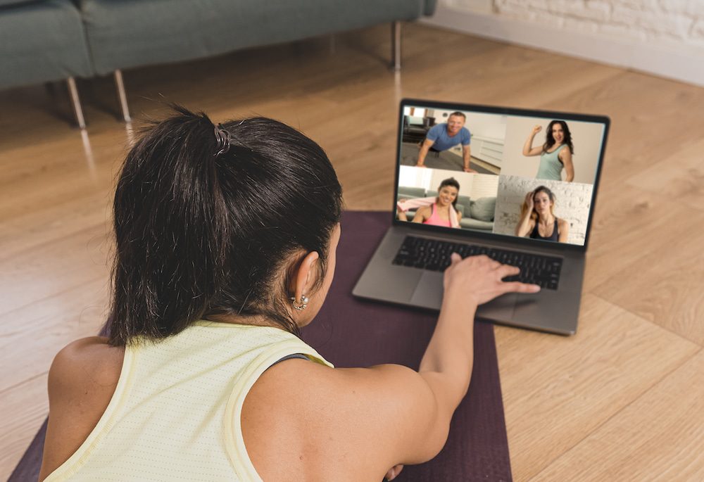 Woman participating in an online group fitness class via laptop at home.