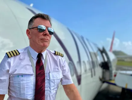 Captain Chris standing beside a commercial aircraft in pilot uniform at the airport.