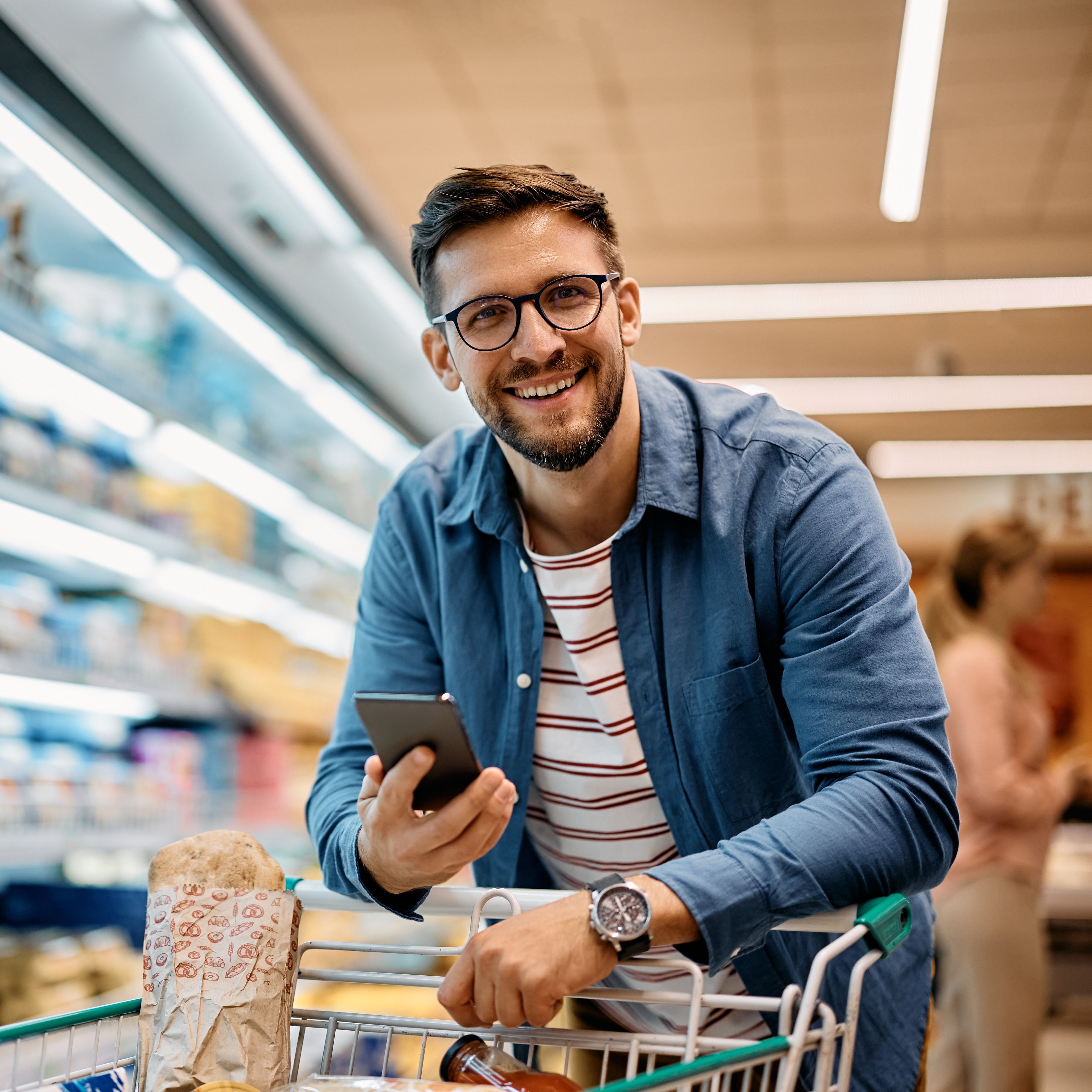 Man with phone smiling and standing in a supermarket.