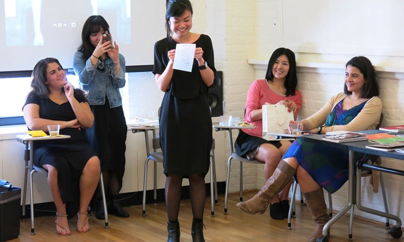 a young woman reading from a piece of paper in front of the class