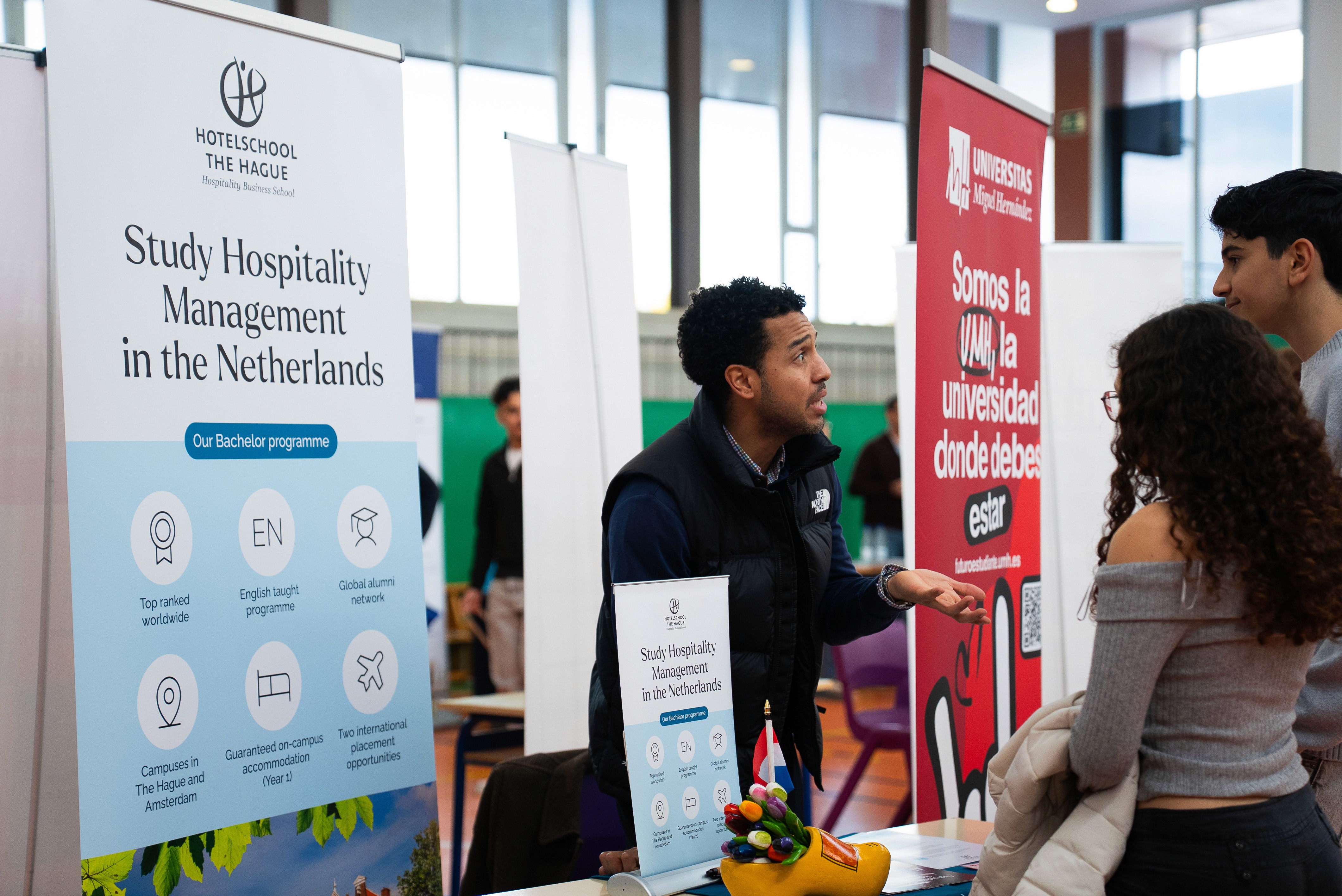 A woman wearing a shiny coat stands in focus, while a blurred background creates a sense of movement.