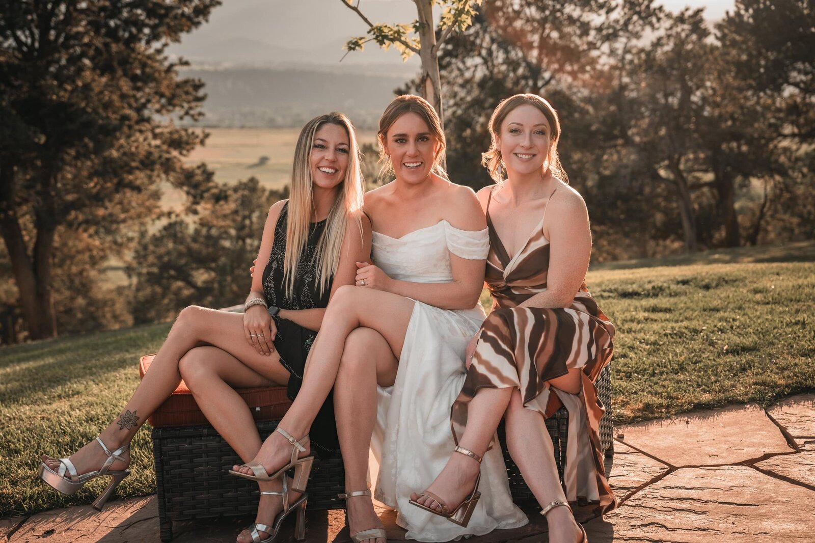 Bride sitting between two guests on a garden bench in warm evening light