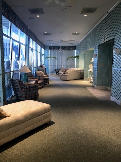A spacious, sunlit lounge featuring comfortable seating with a mix of plaid and floral upholstery, large windows allowing natural light, and green lattice wall accents creating a relaxing ambiance.