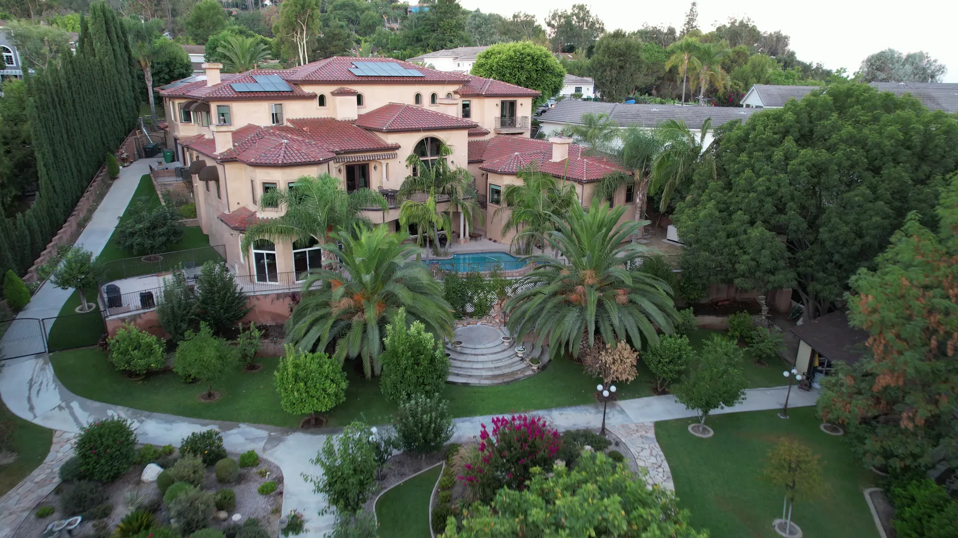 Aerial view of a house, swimming pool, garden paths and palm-lined grounds.