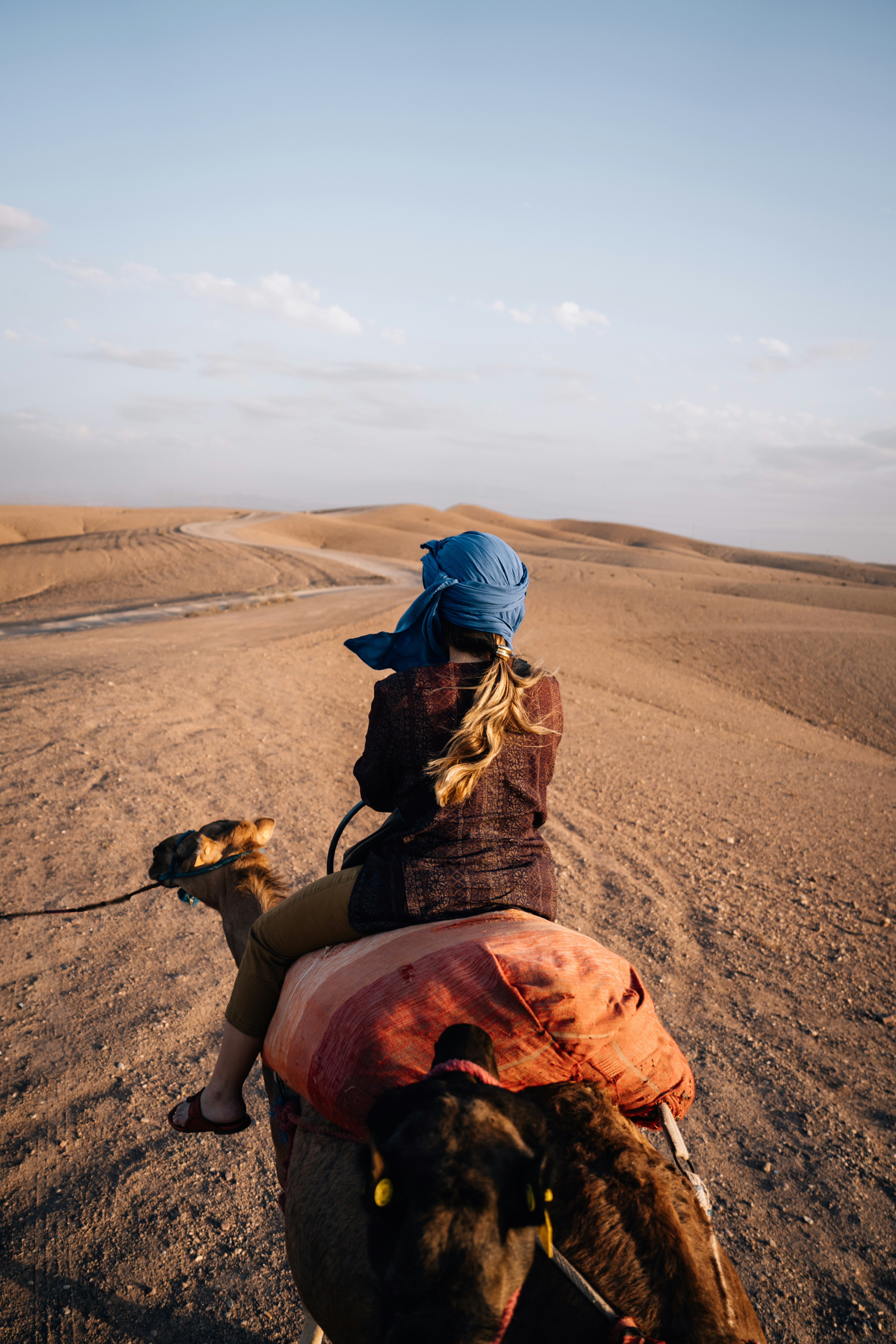 Person riding a camel through desert dunes at sunset.