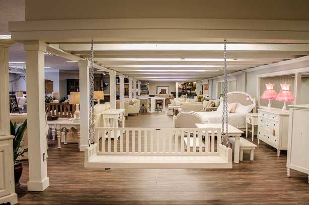 Furniture showroom with focus on a white swinging couch meant for installing on porch.