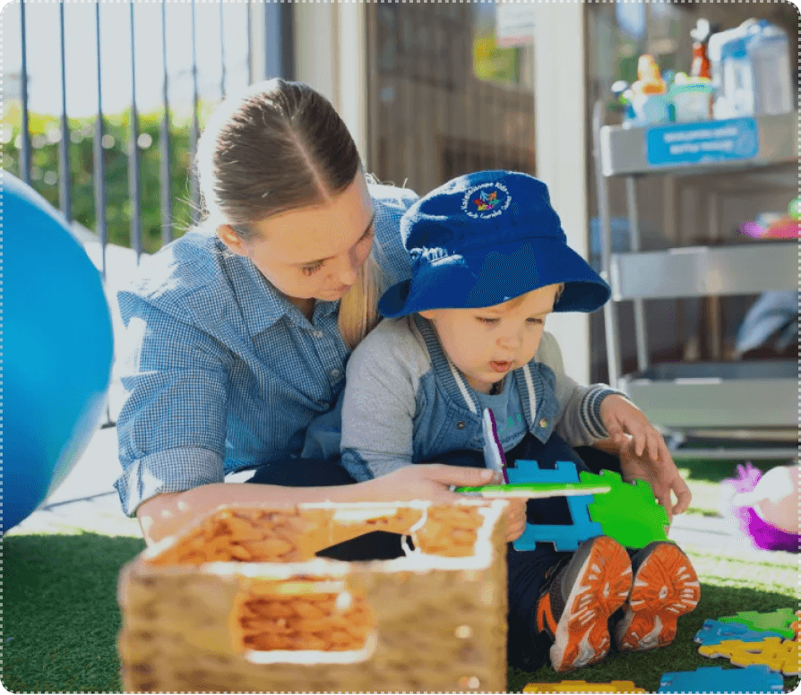 Childcare educator helping a young child with puzzles during play-based learning at Kaleidoscope Kids in Brisbane.