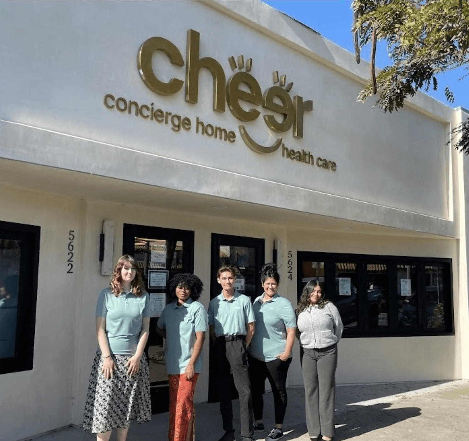 Gold dimensional “Cheer concierge home health care” building sign mounted on a white medical clinic exterior above the entrance with staff standing outside.
