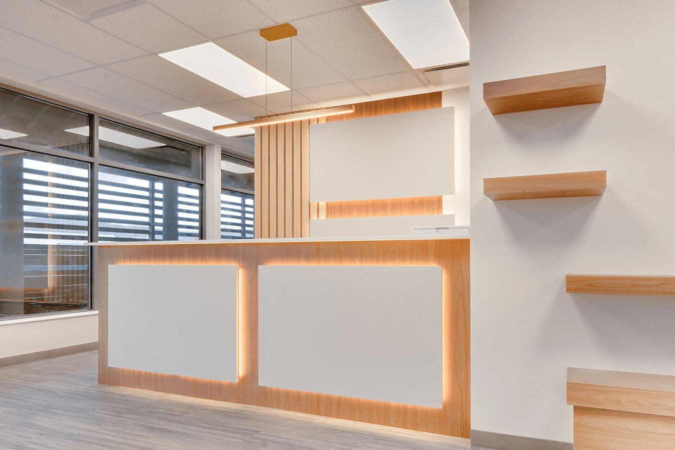 Reception desk and feature wall with integrated lighting, wood slats, and large decorative panels in a bright commercial lobby.