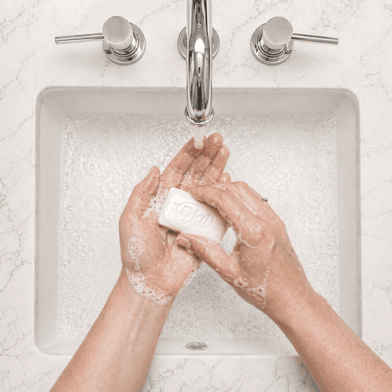 Man washing hands with Dial White Marble soap in a hotel sink from top view with visible branding and running water, by Transmacro Amenities