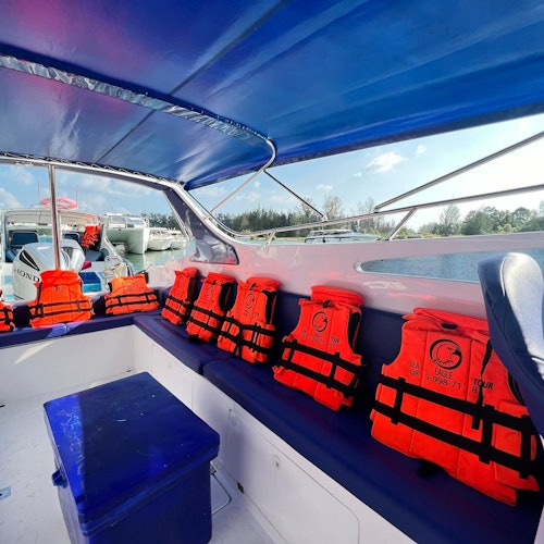 船的内部展示出多个红色救生衣整齐排列在一个蓝色长椅上，长椅位于蓝色遮阳篷下，外面可以看到开阔的水面。