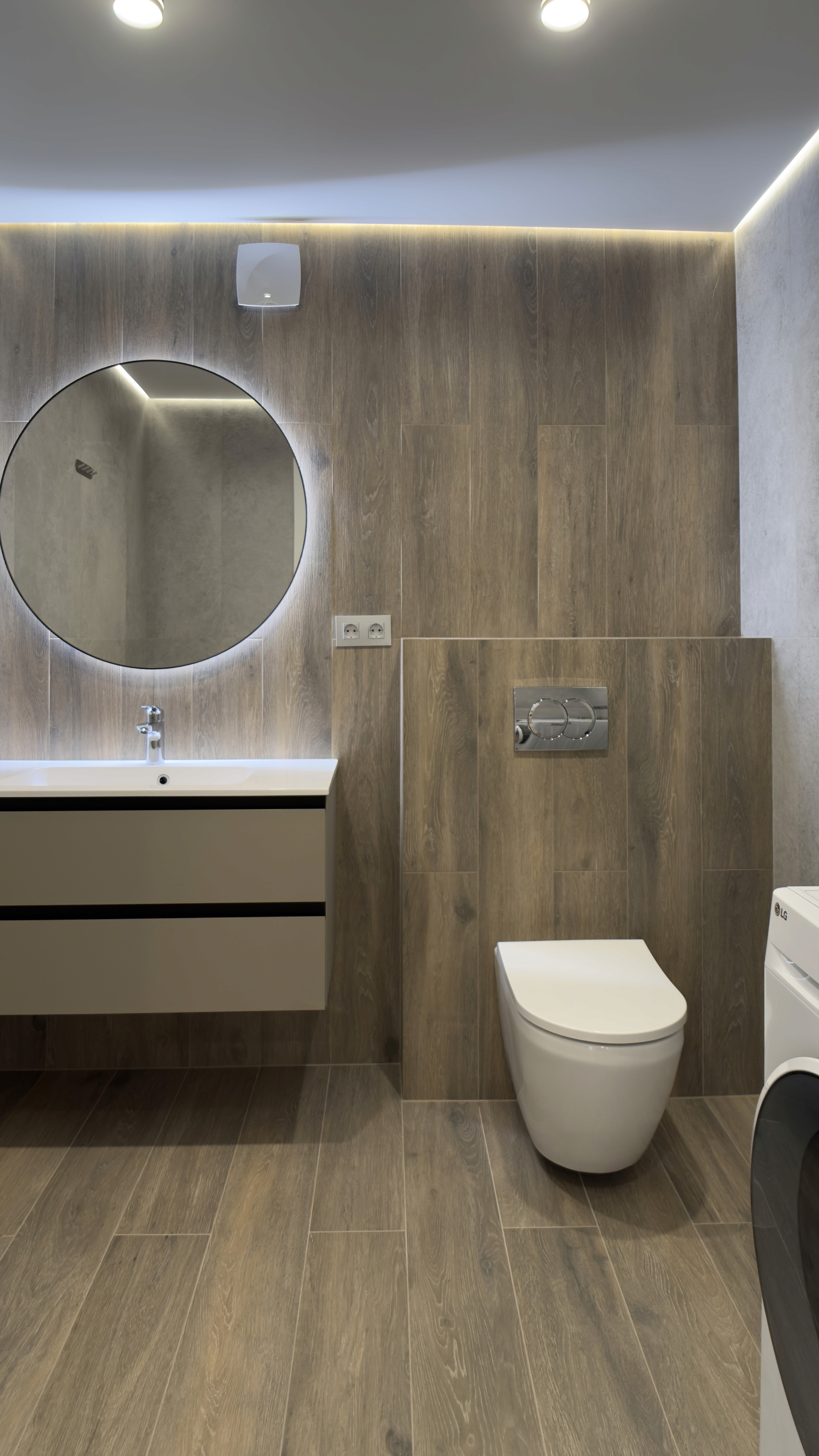 Санвузол з унітазом, пральною машиною, круглим дзеркалом і дерев’яним оздобленням