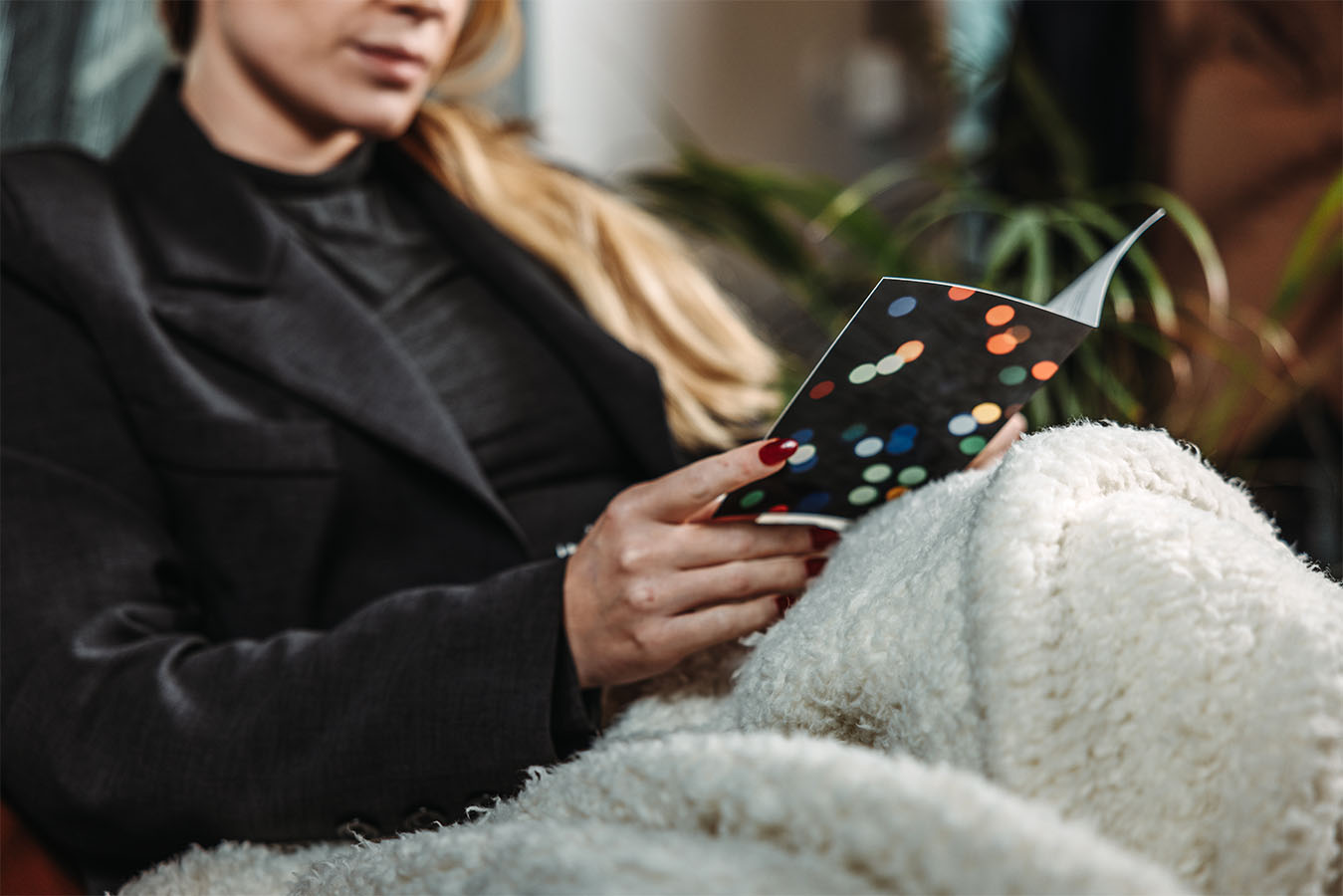 Vrouw gewikkeld in een witte, zachte deken, leest een kaart met kleurrijke stippen