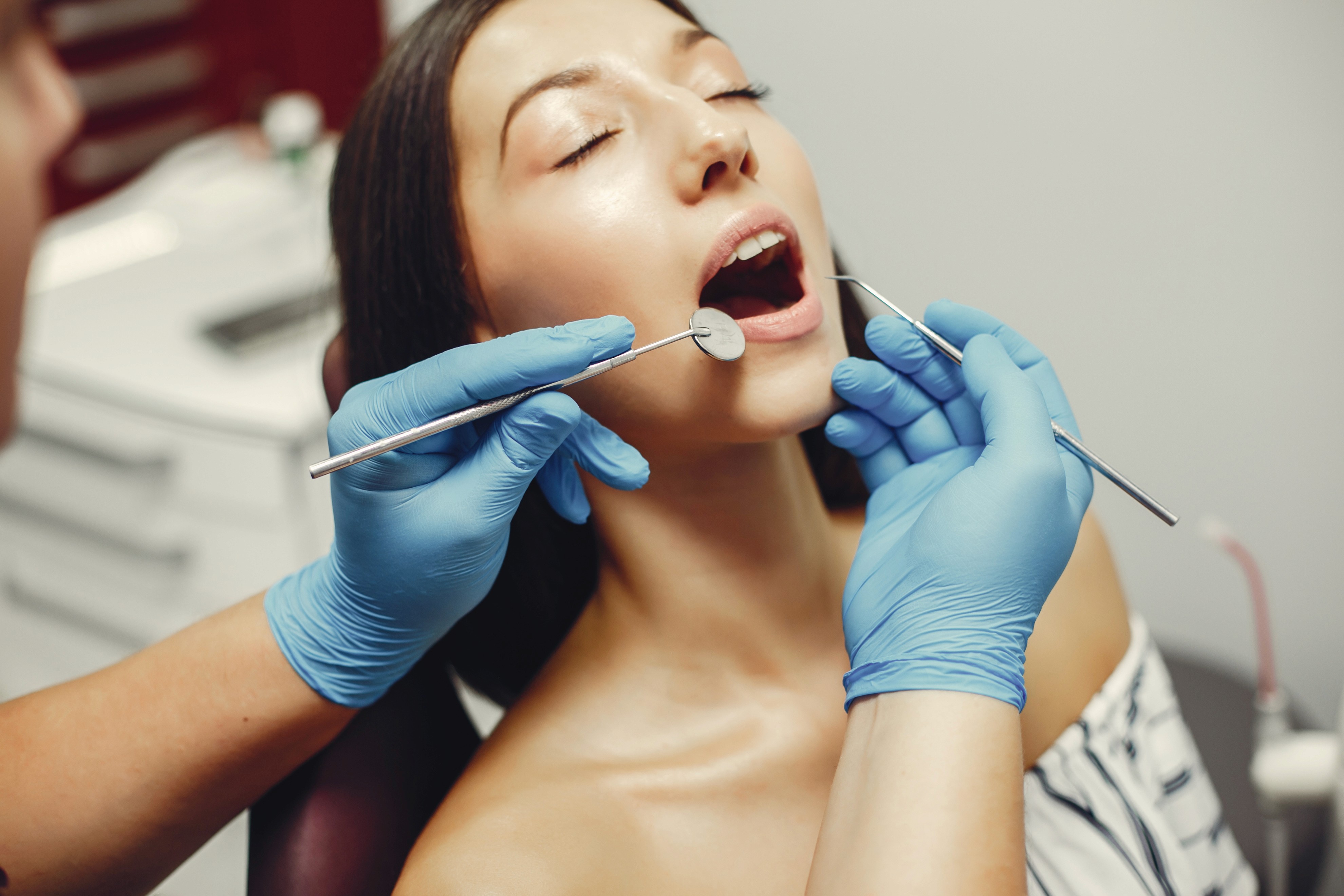 A dental professional using dental instruments to examine a female patient's teeth during a dental procedure.