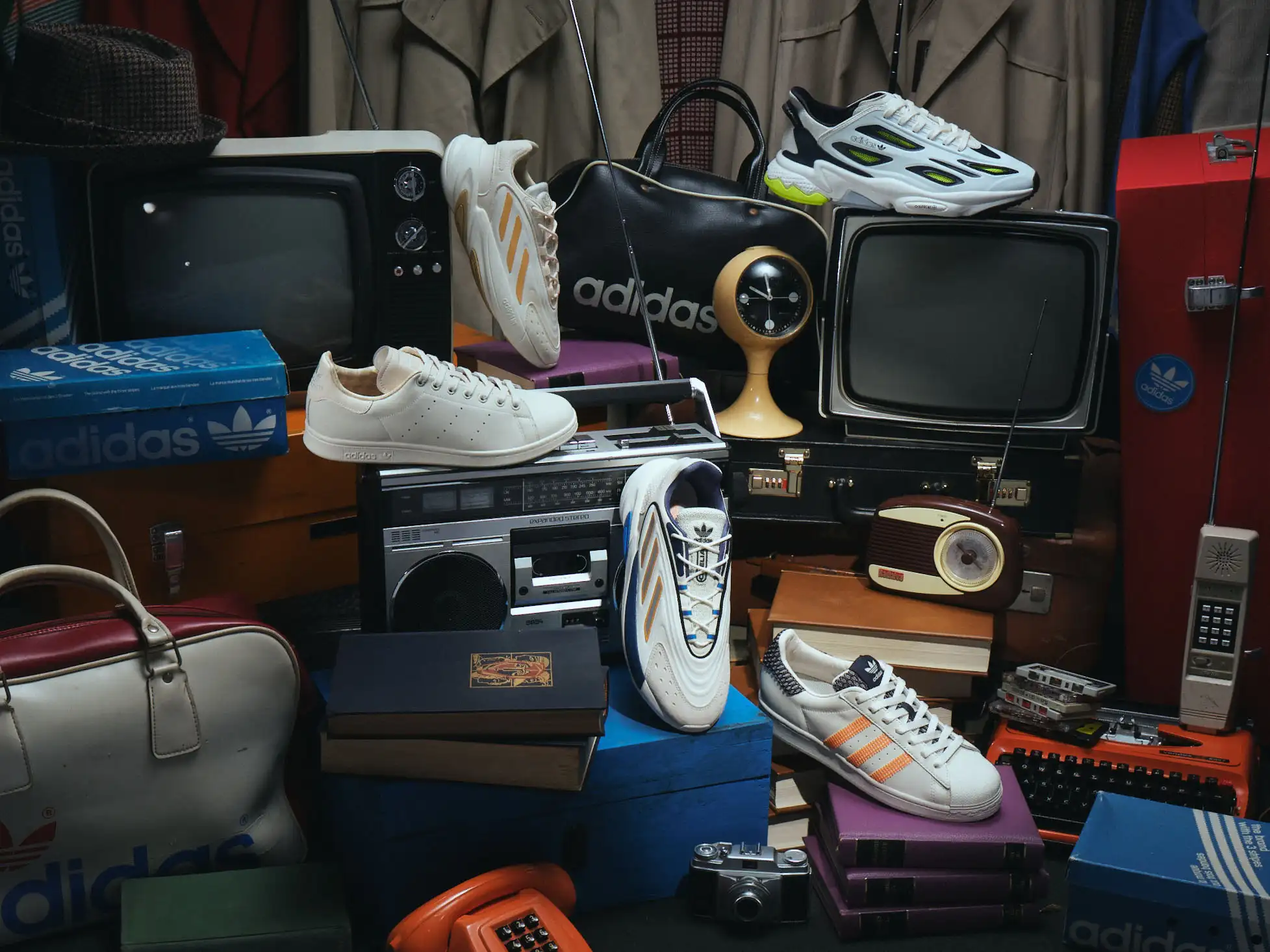 Vintage Adidas sneakers stacked among vintage television sets and travel cases.