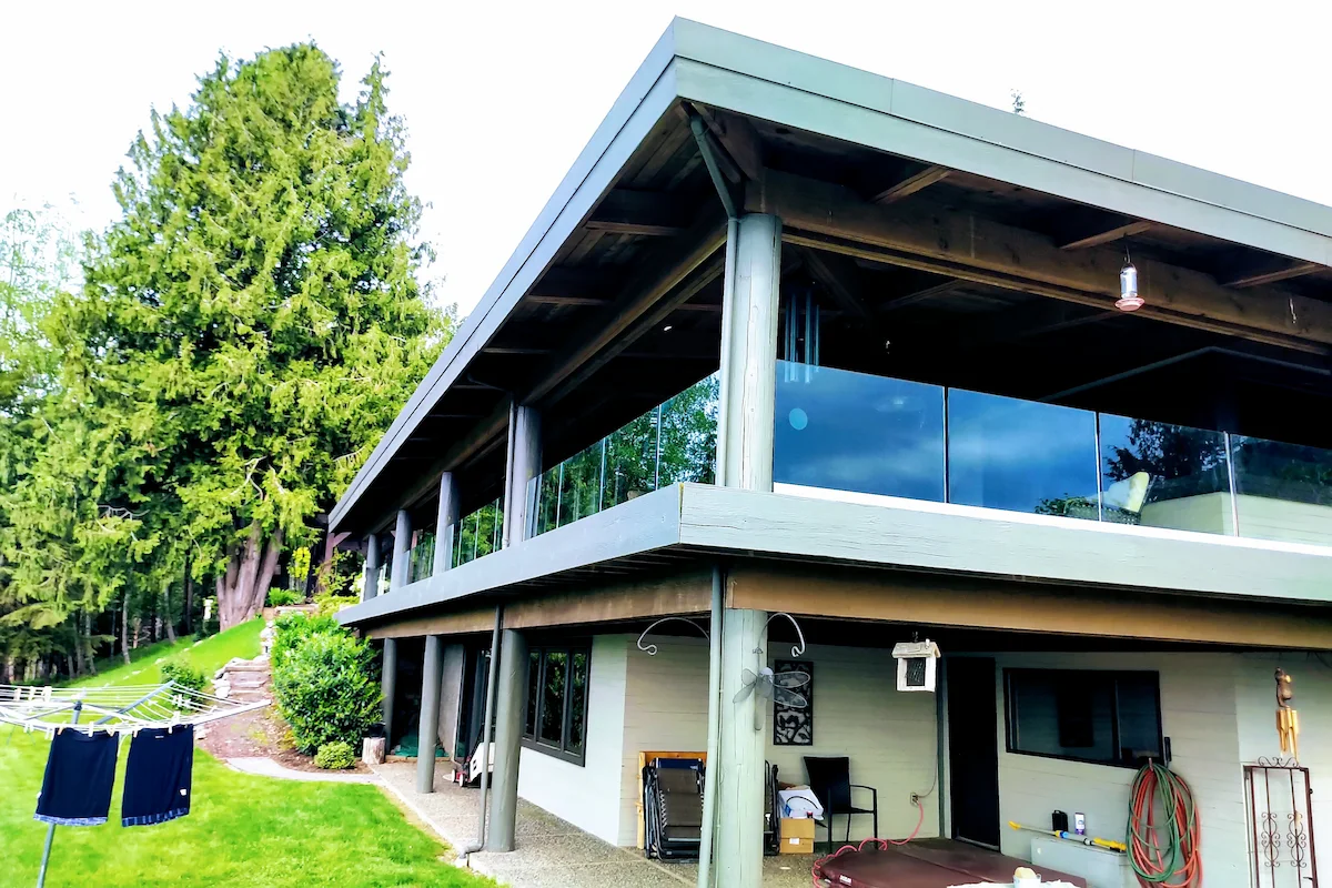Frameless glass balcony installed beneath a modern metal roofline on a contemporary home in the Fraser Valley.