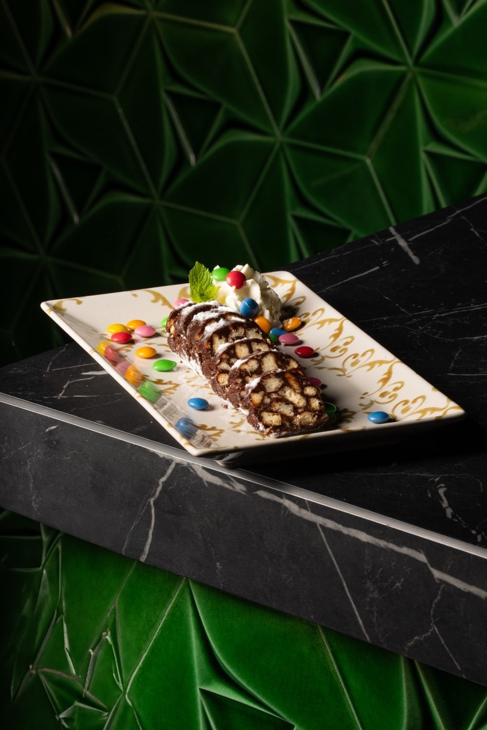 Fette di salame al cioccolato servite con Smarties su vassoio bianco rettangolare