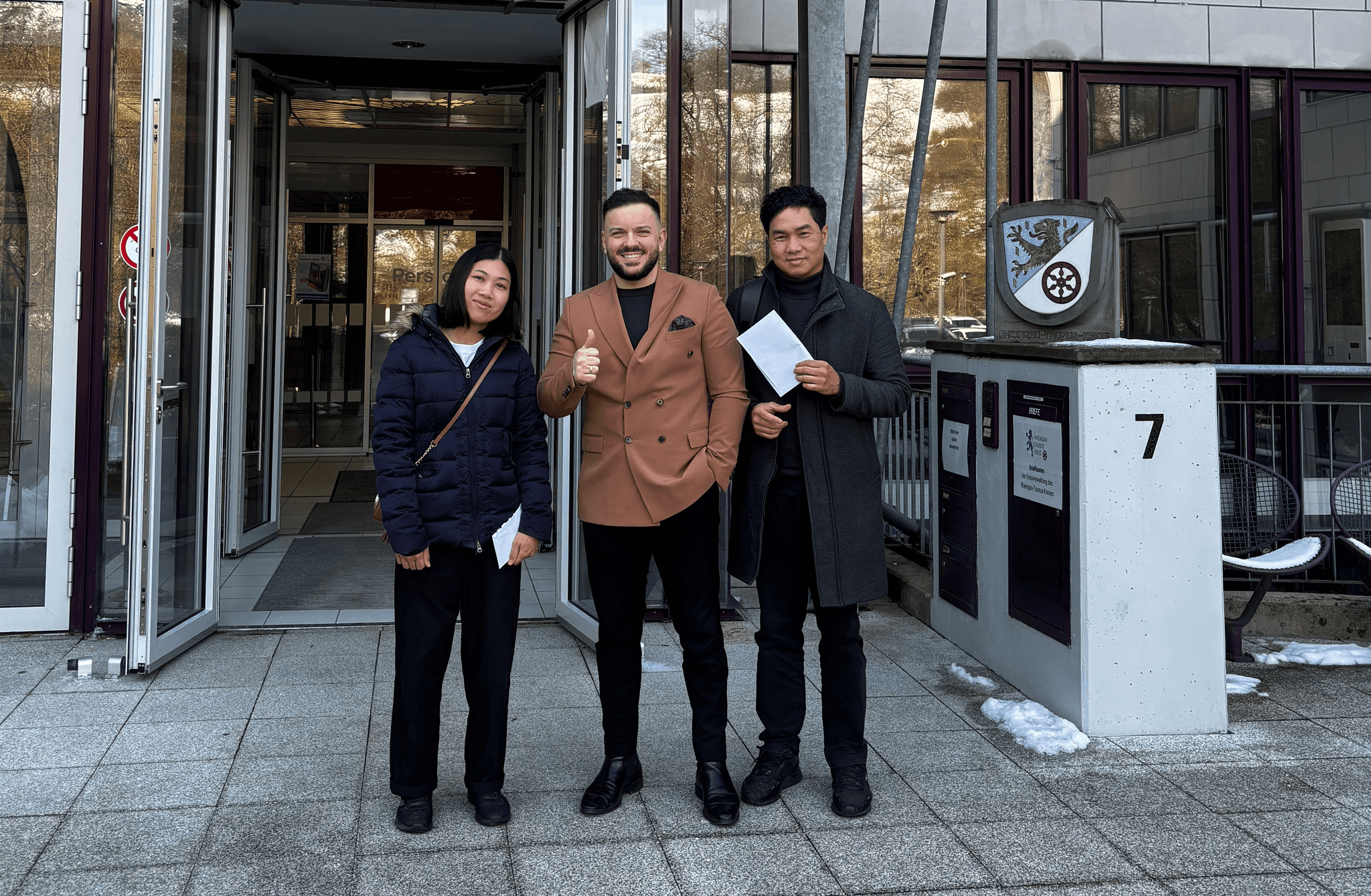 Ben Wassermann von workiOn mit zwei vermittelten Fachkräften vor dem Eingang einer deutschen Ausländerbehörde.